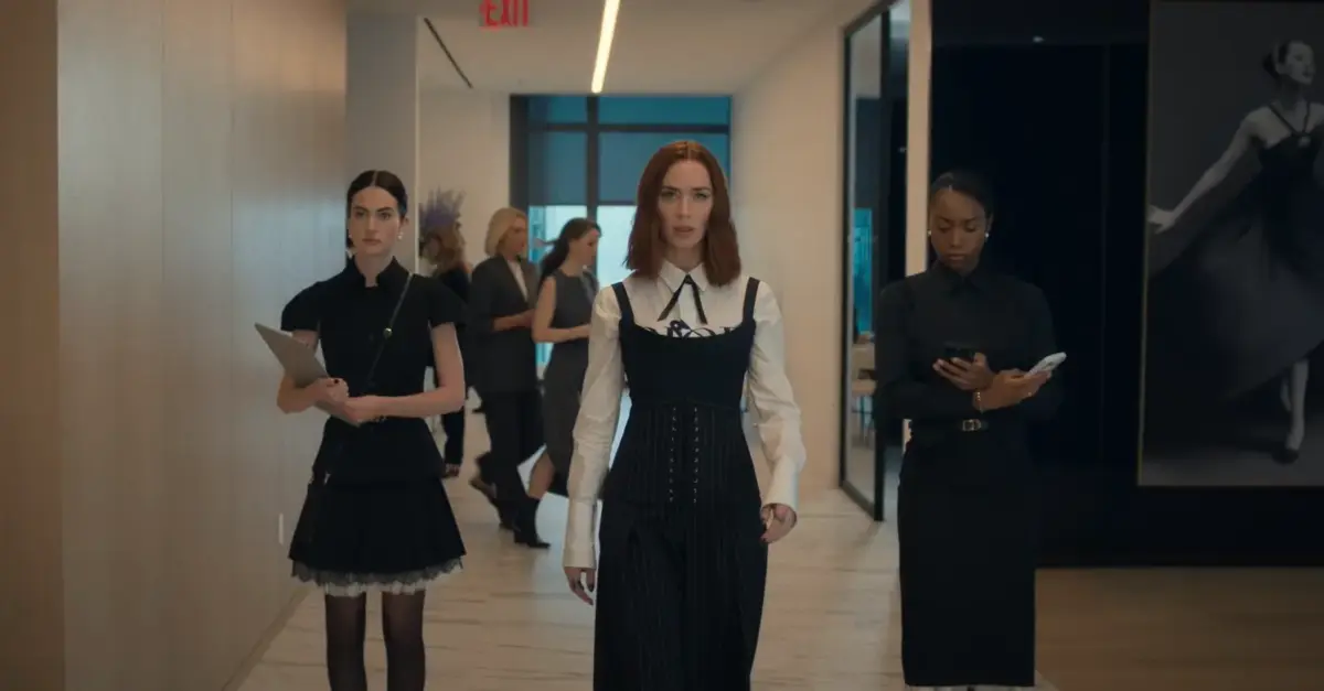 Emily Blunt como Emily Charlton caminha por corredor de escritório moderno com assistentes ao redor, em cena de O Diabo Veste Prada 2