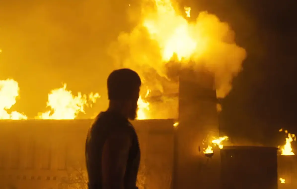 Novo trailer de A Odisseia mostra Odisseu tentando voltar para casa 1 Silhueta de personagem observando cidade em chamas à noite em cena do trailer de A Odisseia de Christopher Nolan