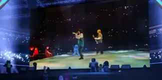 Avatares do Roblox assistem à apresentação de Billie Eilish no The Block, com telão exibindo a cantora no palco durante o evento gratuito de maio de 2026