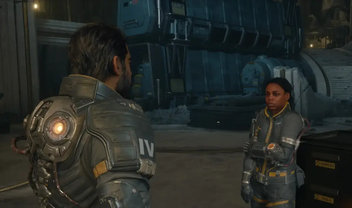 Arjun Debrage de costas conversando com membro da tripulação em área interna da nave em Saros para PS5