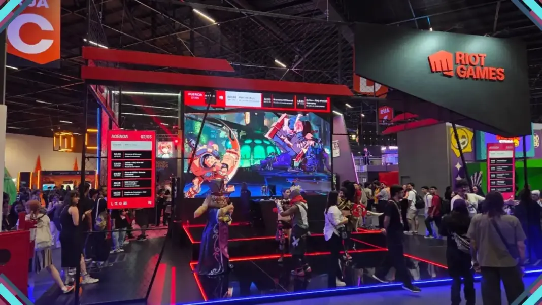 Visão geral do estande da Riot Games na gamescom latam 2026 com telão central exibindo League of Legends, cosplayers no palco e painel de agenda das ativações do dia