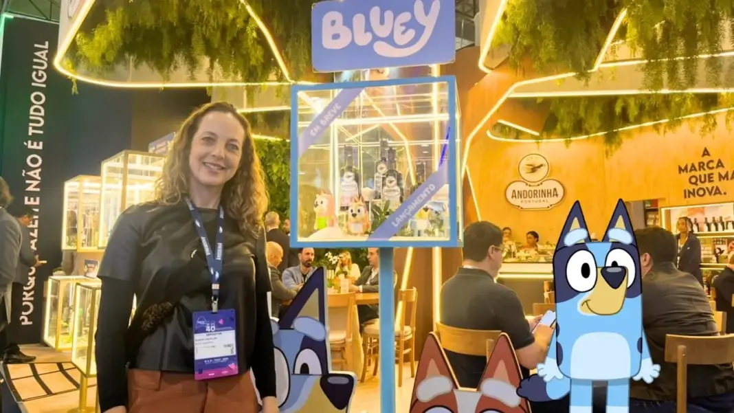 Susan Cavallin posando no estande da Andorinha na APAS Show 2026 com vitrine da edição especial do azeita da Bluey e personagens ao redor