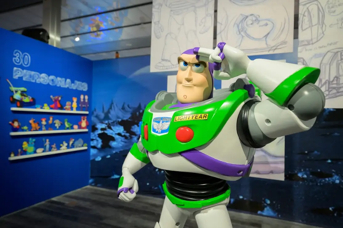 Toy Story ao Infinito e Além: exposição chega a São Paulo em maio 1 Estátua de Buzz Lightyear em destaque com painel de 30 personagens de Toy Story ao fundo na exposição em São Paulo